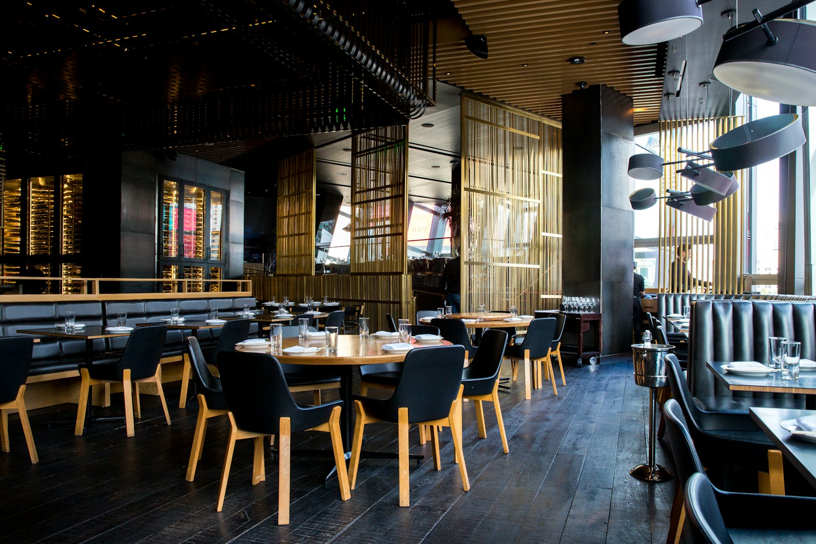 Warmly lit restaurant interior with wood tables, green foliage, and a welcoming bar